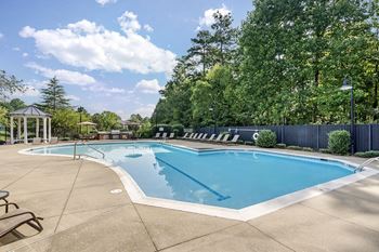 A large outdoor swimming pool surrounded by trees and a fence.
